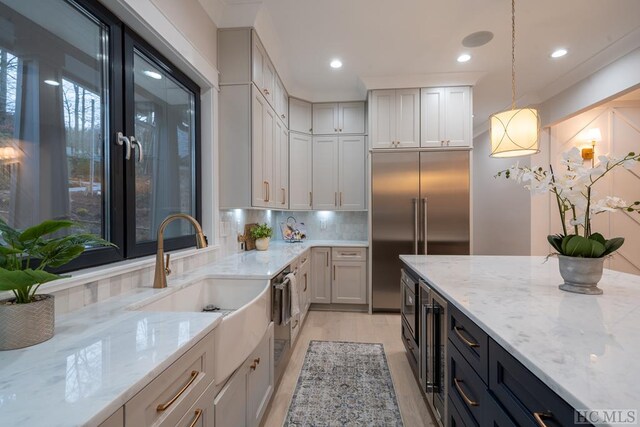 kitchen featuring sink, hanging light fixtures, tasteful backsplash, built in appliances, and light stone countertops