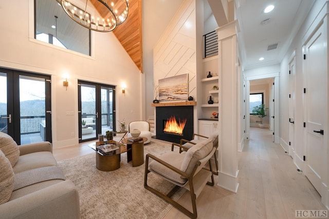 living room featuring an inviting chandelier, a towering ceiling, light hardwood / wood-style floors, french doors, and built in features