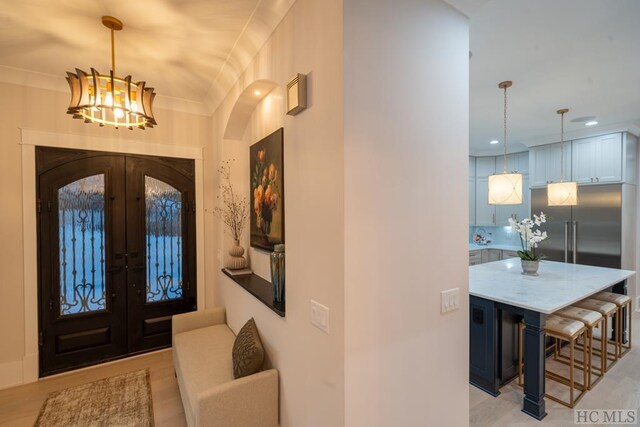 foyer entrance with french doors, ornamental molding, and an inviting chandelier