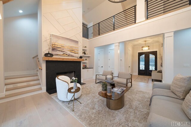 living room with french doors, light hardwood / wood-style floors, built in features, and a high ceiling