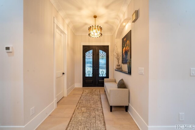 foyer entrance with french doors, ornamental molding, a chandelier, and light wood-type flooring