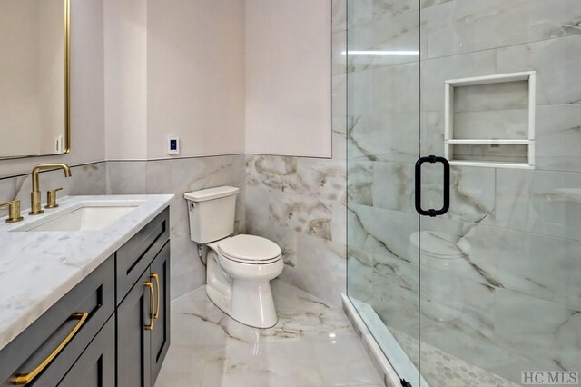 bathroom featuring vanity, toilet, a shower with door, and tile walls