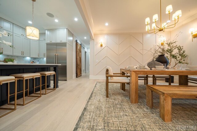 dining room with a barn door, a chandelier, and light hardwood / wood-style floors