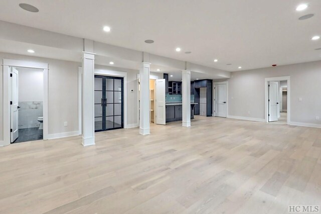 unfurnished living room featuring ornate columns and light wood-type flooring