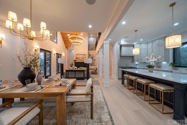 dining room featuring lofted ceiling, an inviting chandelier, light hardwood / wood-style floors, wooden ceiling, and ornate columns