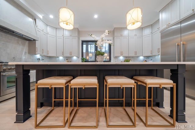 kitchen featuring premium range hood, hanging light fixtures, decorative backsplash, and white cabinets