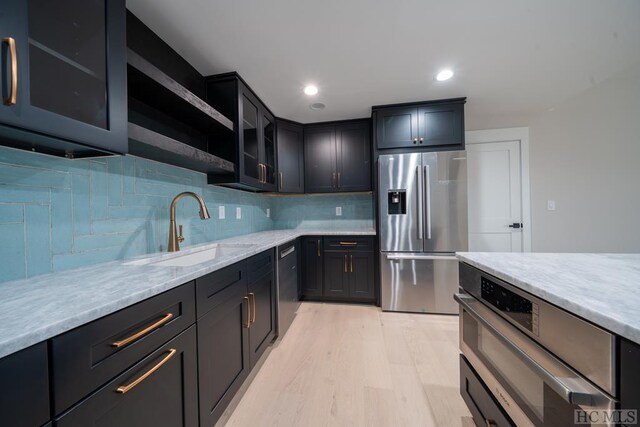 kitchen with appliances with stainless steel finishes, light stone countertops, light hardwood / wood-style floors, backsplash, and sink