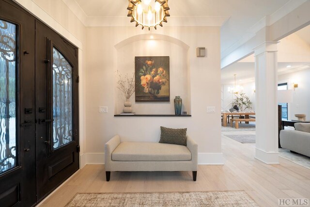 entrance foyer featuring decorative columns, an inviting chandelier, ornamental molding, plenty of natural light, and light hardwood / wood-style floors