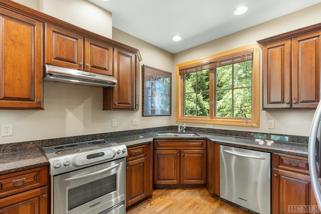 kitchen featuring sink, dark stone countertops, light wood-type flooring, and stainless steel appliances