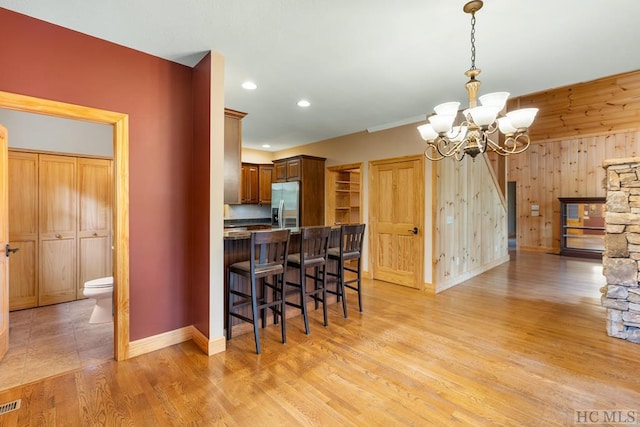 kitchen with wood walls, stainless steel fridge, a kitchen bar, a notable chandelier, and light wood-type flooring