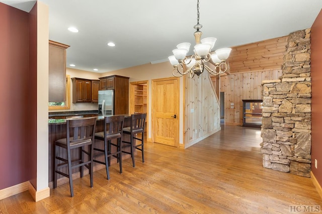 kitchen featuring a breakfast bar, wooden walls, stainless steel fridge with ice dispenser, kitchen peninsula, and a chandelier