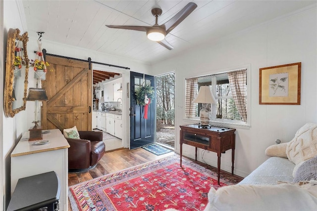 living room featuring a barn door, a ceiling fan, wood ceiling, ornamental molding, and light wood-style floors