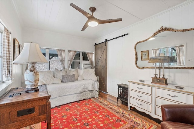 bedroom with ornamental molding, a barn door, and wood finished floors