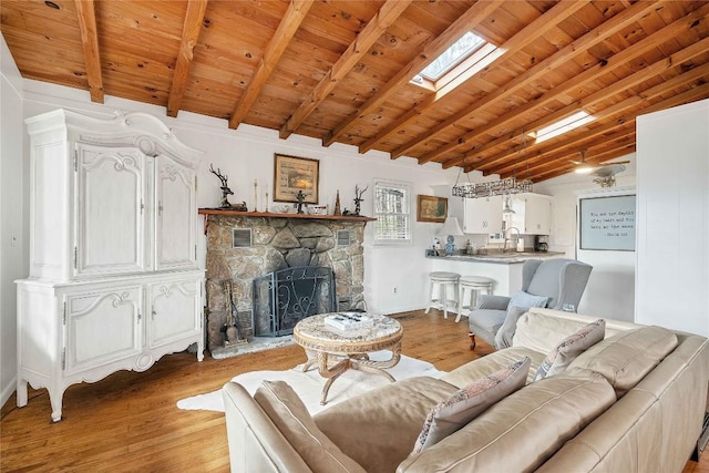 living room with light wood-style floors, vaulted ceiling with skylight, wood ceiling, and a fireplace