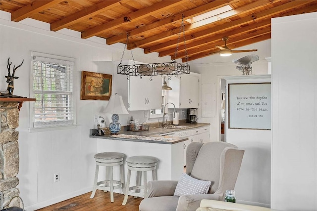 kitchen with vaulted ceiling with beams, wood ceiling, white cabinetry, a sink, and wood finished floors