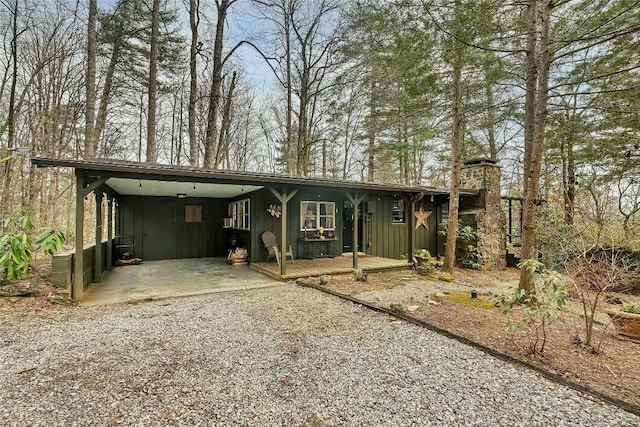 view of front of home featuring board and batten siding, a chimney, gravel driveway, and a carport