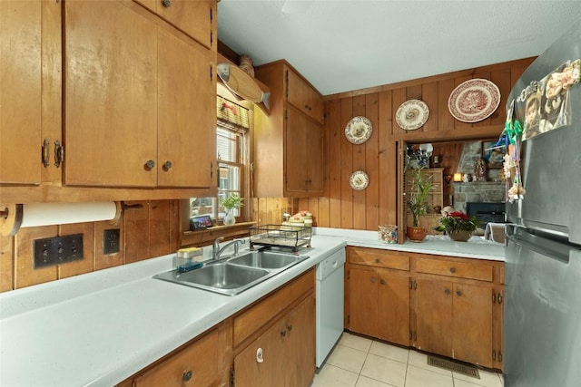 kitchen featuring light tile patterned flooring, wooden walls, stainless steel refrigerator, dishwasher, and sink