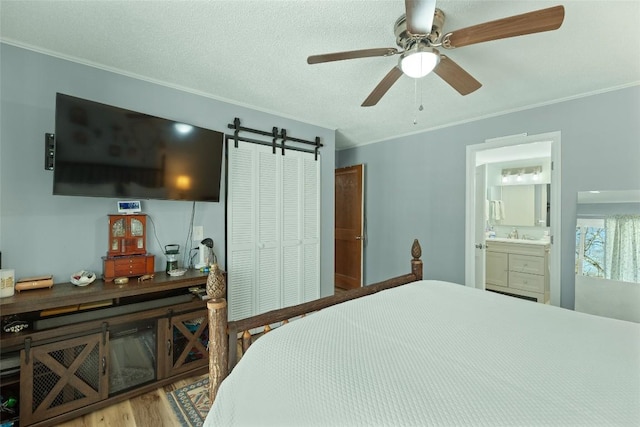 bedroom with connected bathroom, light hardwood / wood-style flooring, ceiling fan, a barn door, and a closet