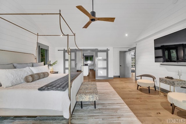 bedroom featuring lofted ceiling, ceiling fan, wood-type flooring, a barn door, and wood walls