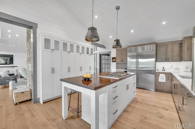 kitchen with lofted ceiling, appliances with stainless steel finishes, white cabinets, decorative light fixtures, and light wood-type flooring