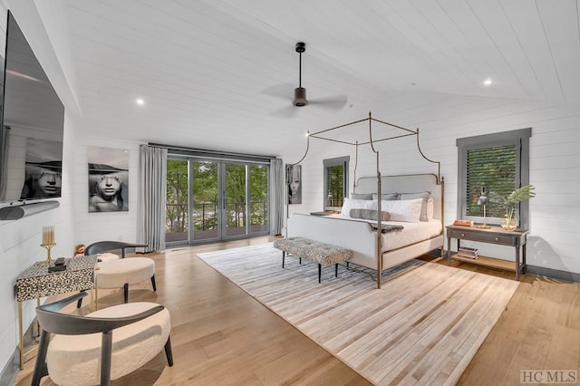 bedroom with access to exterior, vaulted ceiling, light hardwood / wood-style flooring, and wood walls