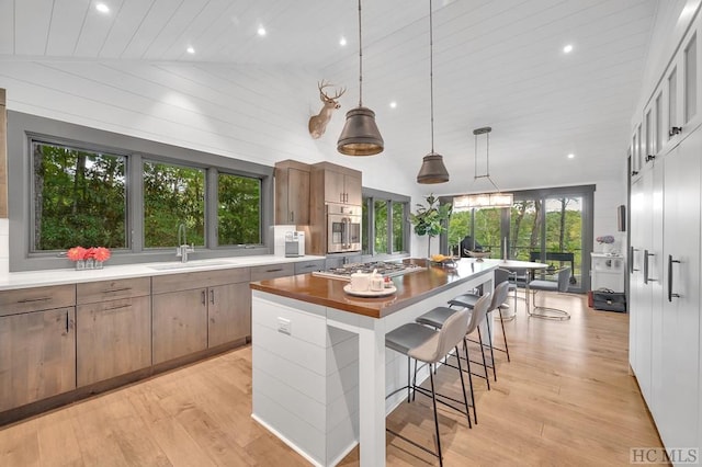 kitchen with pendant lighting, high vaulted ceiling, sink, a center island, and light hardwood / wood-style floors