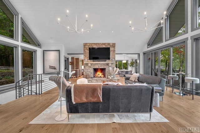 living room with an inviting chandelier, high vaulted ceiling, a stone fireplace, and light hardwood / wood-style floors