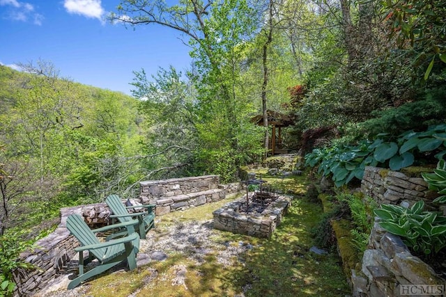 view of yard featuring a fire pit and a view of trees