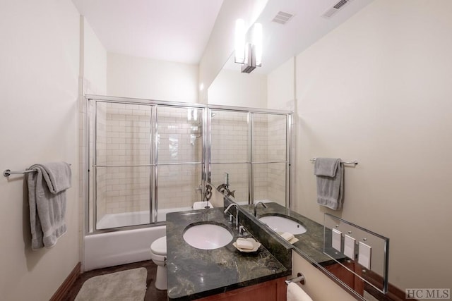 bathroom with visible vents, vanity, toilet, and bath / shower combo with glass door