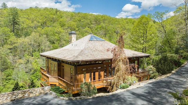 exterior space with covered porch, a forest view, and a chimney