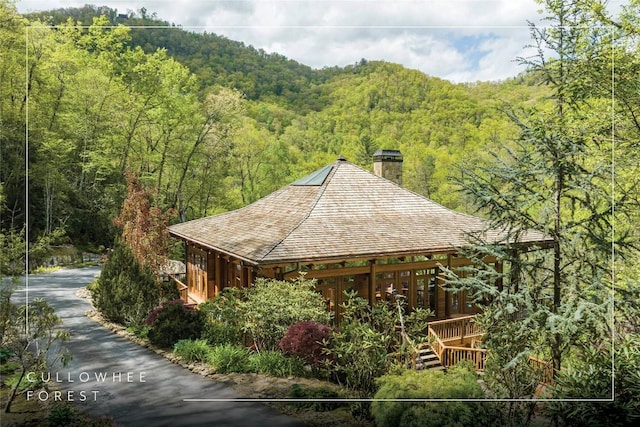 exterior space with a deck, a wooded view, and a chimney