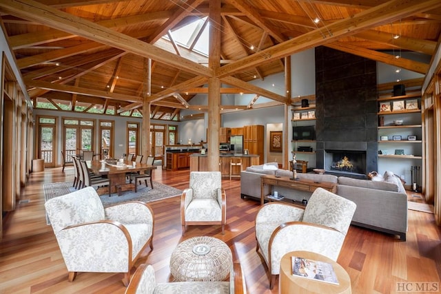 living area with beam ceiling, wood ceiling, a large fireplace, and light wood finished floors