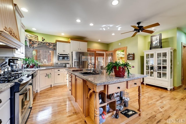 kitchen with a kitchen island, premium range hood, sink, light stone counters, and appliances with stainless steel finishes