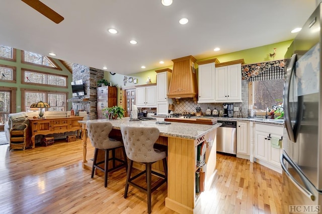 kitchen with a center island, light stone countertops, custom range hood, appliances with stainless steel finishes, and white cabinets