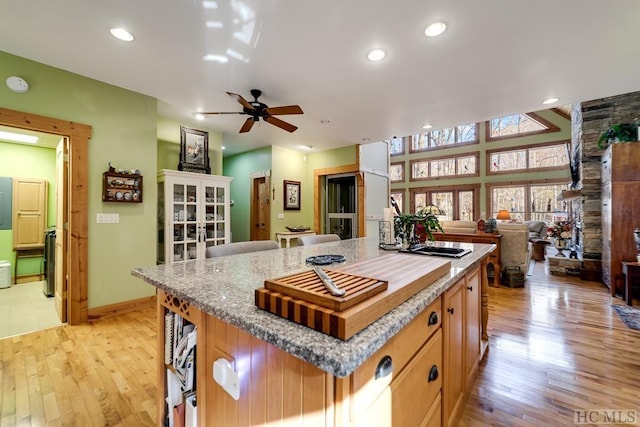 kitchen with light wood-type flooring, a center island, ceiling fan, french doors, and light stone countertops