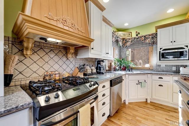 kitchen with appliances with stainless steel finishes, light hardwood / wood-style flooring, tasteful backsplash, premium range hood, and white cabinets