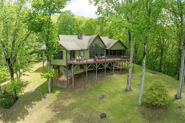 back of property with a wooden deck, a sunroom, a yard, roof with shingles, and a chimney