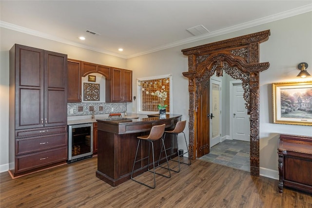 kitchen featuring wine cooler, dark wood-style floors, a breakfast bar area, decorative backsplash, and crown molding