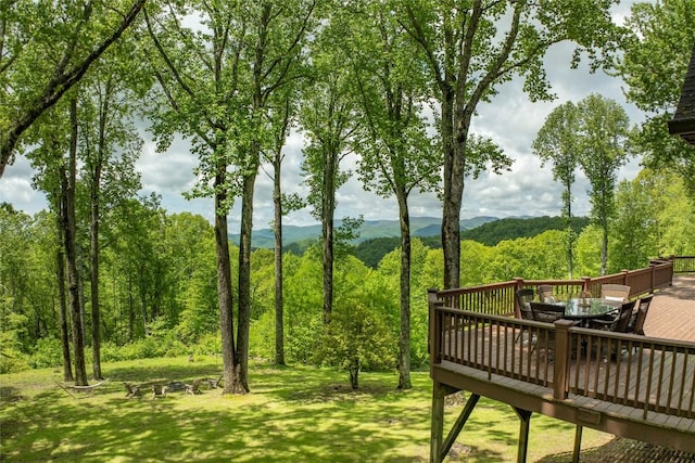 view of property's community featuring outdoor dining area, a deck, a wooded view, and a yard