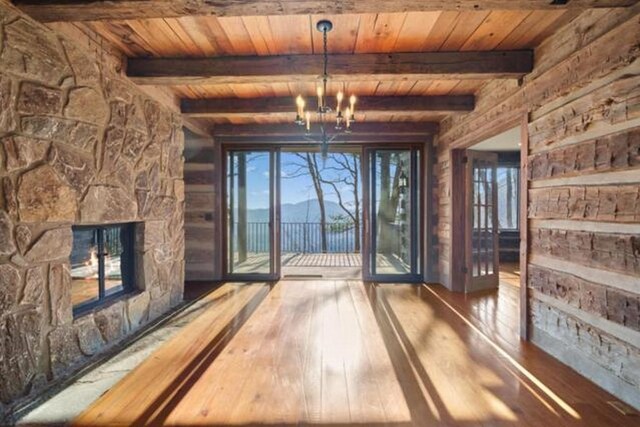 69 Old Cove Rd, Highlands, NC 28741 - unfurnished living room featuring wooden ceiling with exposed beams, wood-type flooring, a chandelier, and a stone fireplace