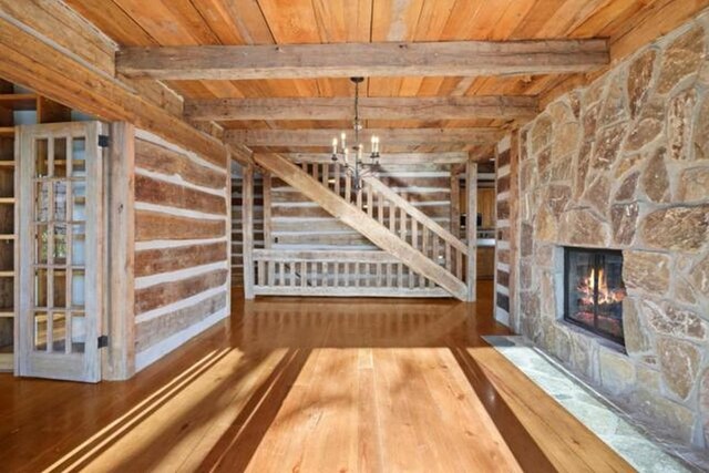 69 Old Cove Rd, Highlands, NC 28741 - unfurnished living room with wood ceiling with exposed beams, hardwood / wood-style floors, a chandelier, and a stone fireplace
