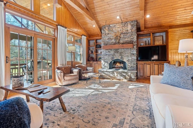 living room with built in shelves, beamed ceiling, wood walls, a stone fireplace, and wooden ceiling