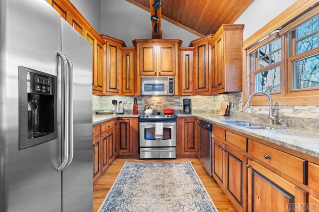 kitchen featuring stainless steel appliances, light stone countertops, lofted ceiling, decorative backsplash, and sink