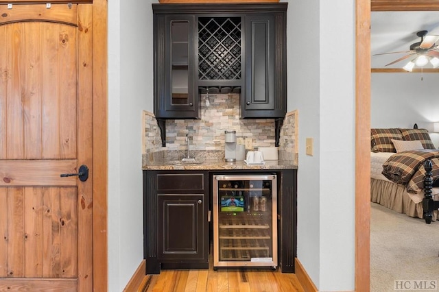 bar with sink, beverage cooler, light hardwood / wood-style floors, light stone countertops, and decorative backsplash