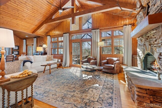 living room featuring light hardwood / wood-style flooring, wood walls, wooden ceiling, a fireplace, and beam ceiling