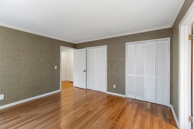 unfurnished bedroom featuring hardwood / wood-style flooring, ornamental molding, and two closets