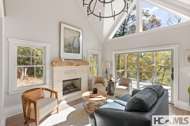 living area featuring wood finished floors, high vaulted ceiling, a stone fireplace, a chandelier, and baseboards