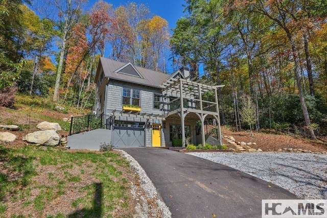 view of front of house with a pergola, an attached garage, driveway, and metal roof