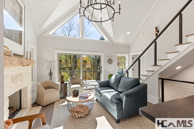 living area featuring a chandelier, wood finished floors, stairway, a fireplace with raised hearth, and high vaulted ceiling