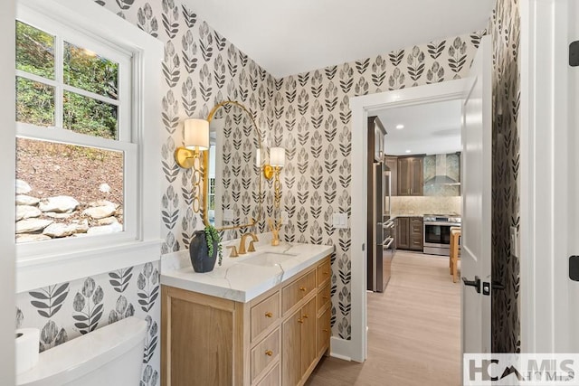 half bathroom featuring wallpapered walls, toilet, vanity, wood finished floors, and recessed lighting